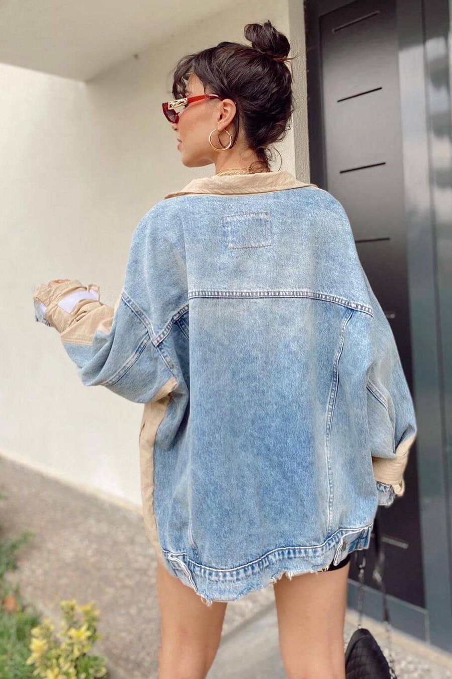 Woman wearing a light blue denim jacket and beige top, standing outside a building.