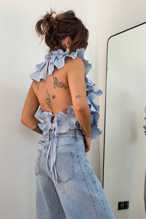 Person wearing a light blue denim outfit with ruffled top in a room.