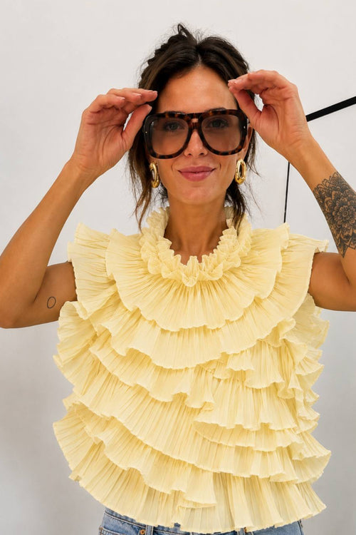 Woman wearing a yellow ruffled top and blue jeans against a white background