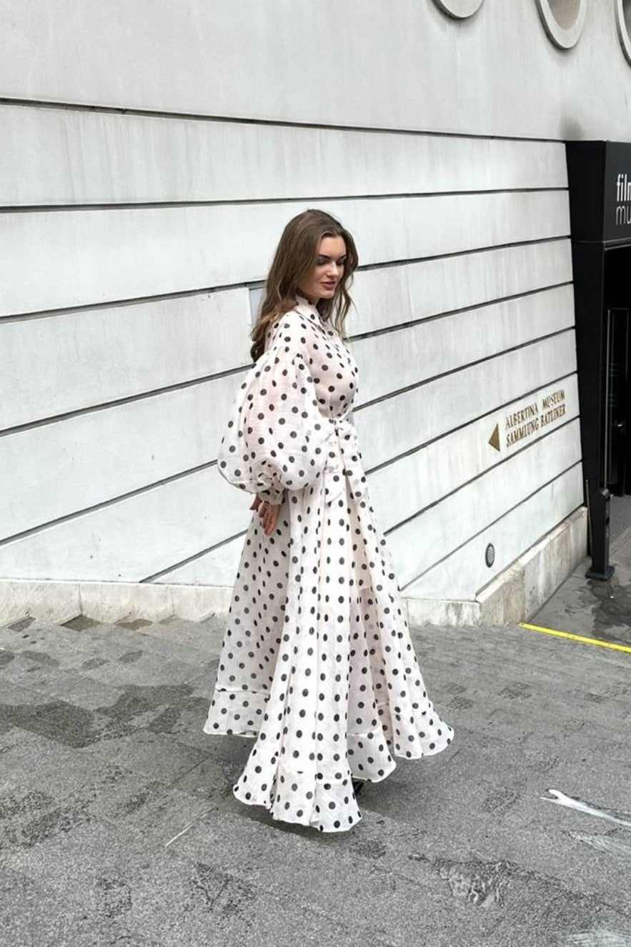 Woman in a polka dot dress standing in front of a modern building with circular windows.