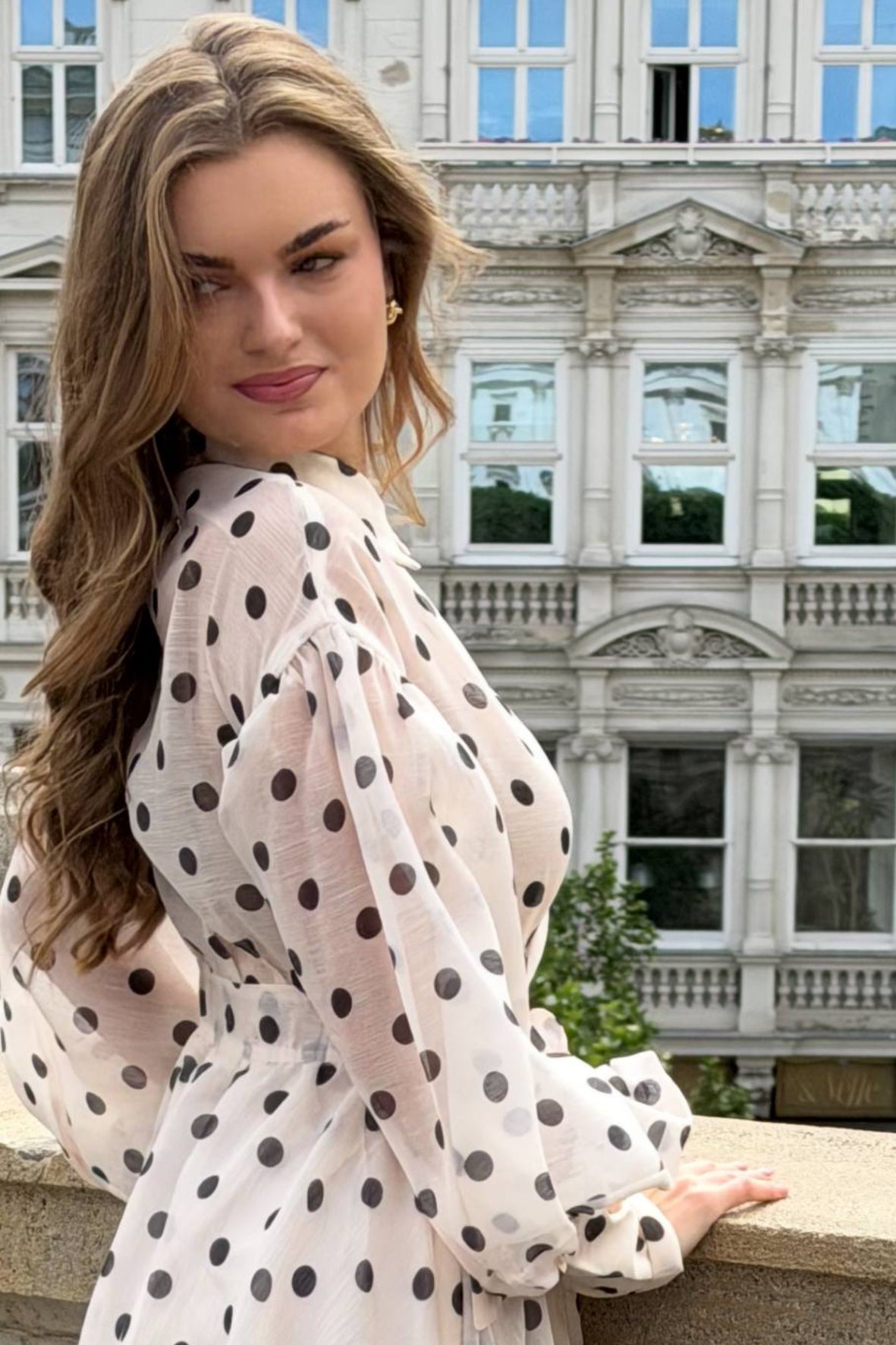 Woman in a polka dot dress standing in front of an elegant building.