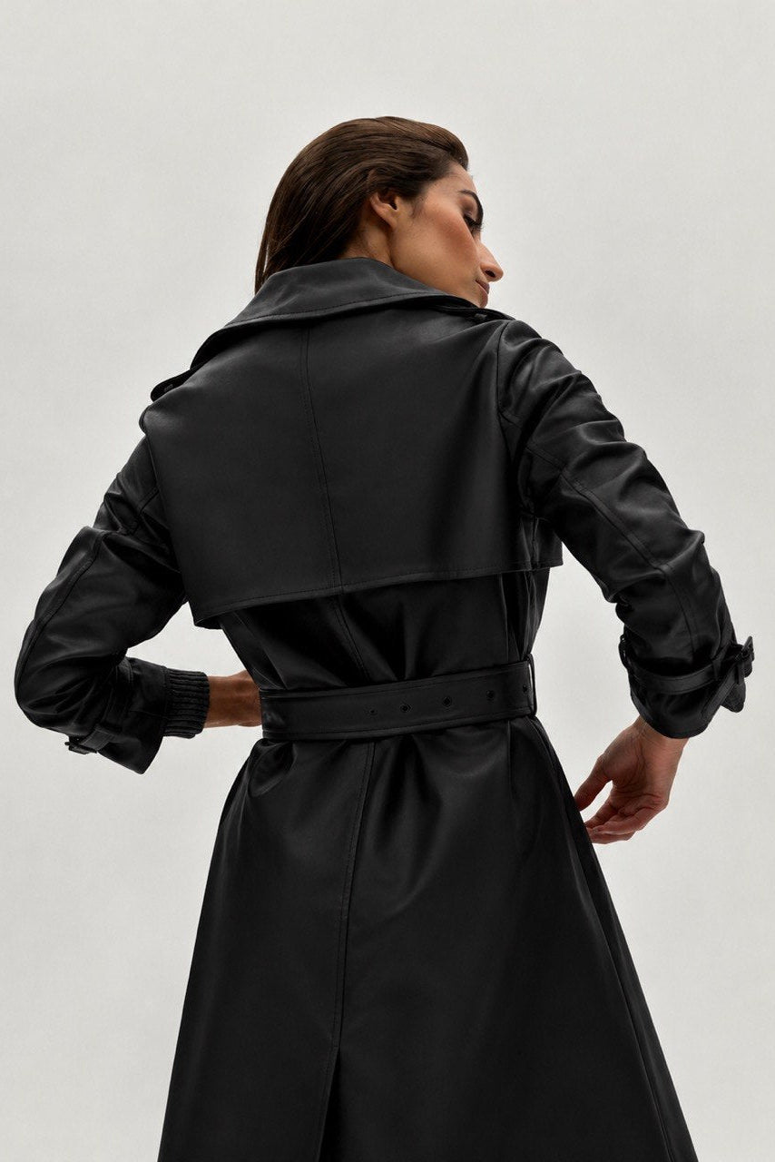 Person wearing a black trench coat on a plain background