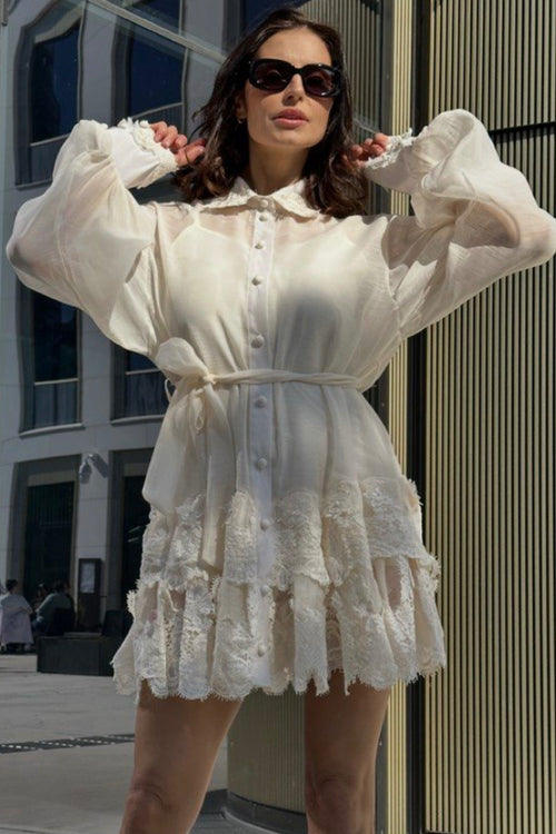 Woman wearing a white dress with ruffled sleeves and skirt in an urban setting.