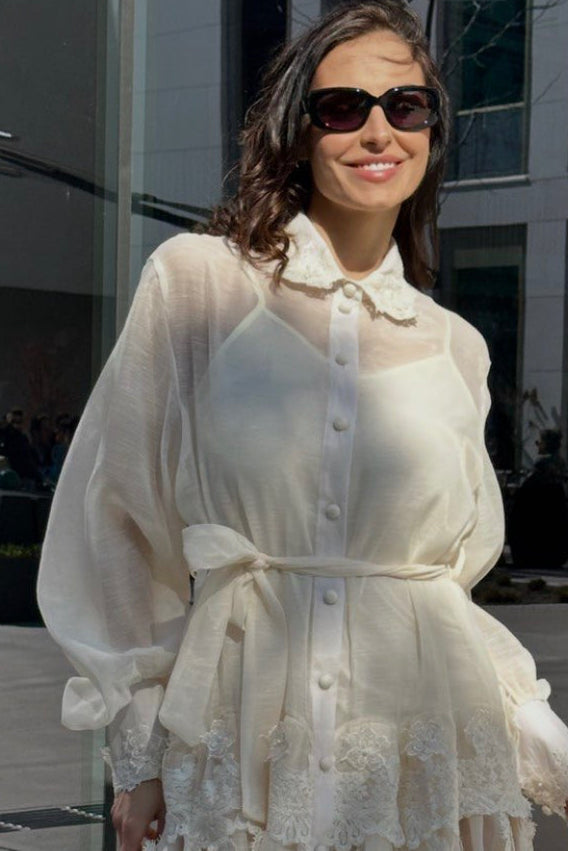 Woman wearing a white lace dress with sunglasses outdoors.