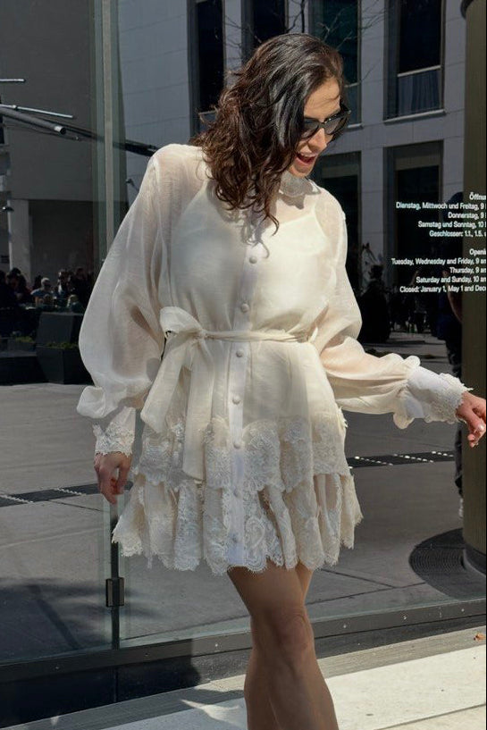 Woman in a white dress standing on a city street.