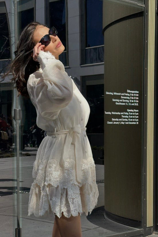 Woman in a white lace dress standing on a city street.